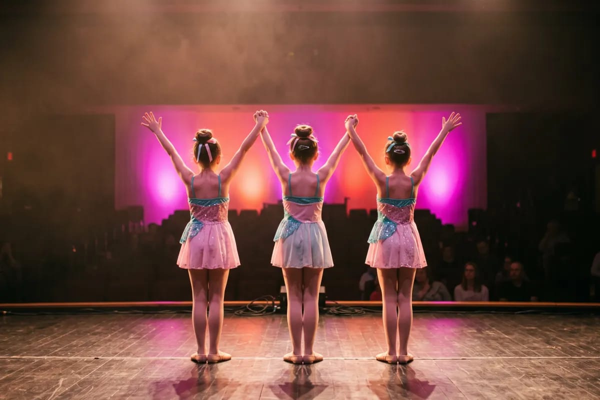 Three dancers seen from behind taking a finale pose under magenta stage lights