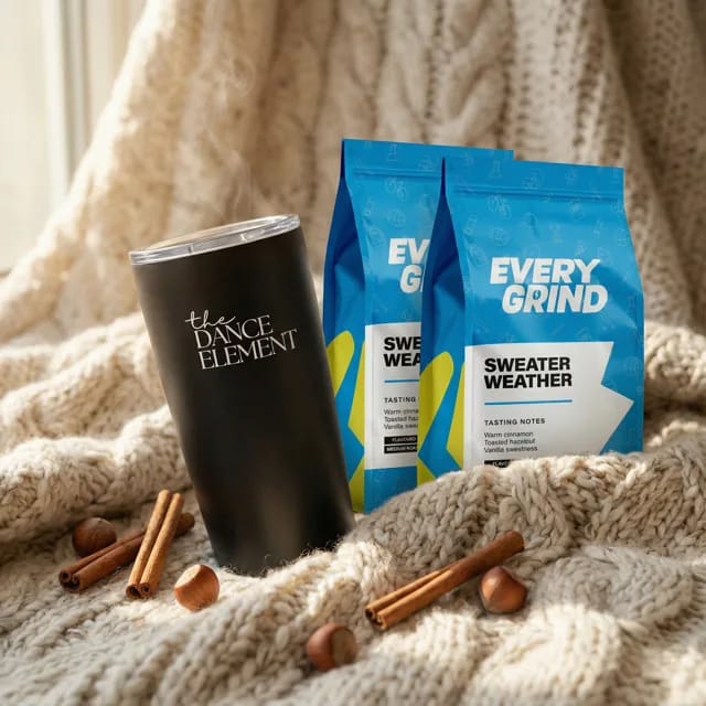 A studio-branded stainless steel travel tumbler beside two bags of Everygrind Sweater Weather coffee